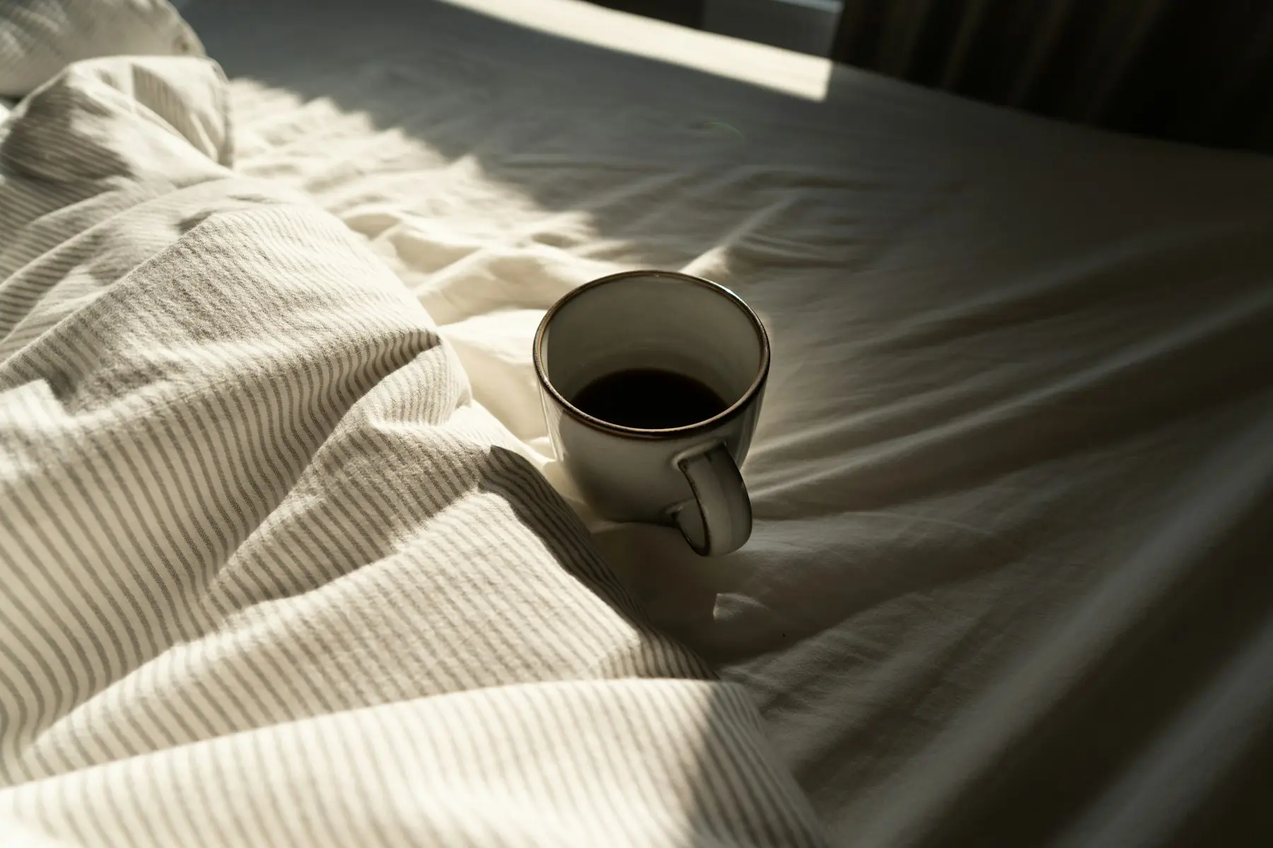 A mug of coffee resting on the rumpled bedding